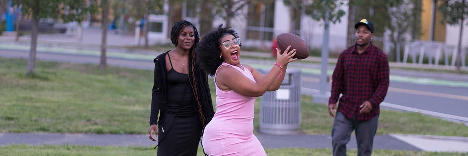 在第一个星期五的活动校园中心草坪上，穿着粉红色连衣裙的女孩抓住了足球.